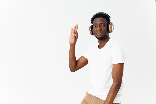 Afro-Amerikaan in koptelefoon in een wit t-shirt luistert naar muziek handgebaar lichte achtergrond