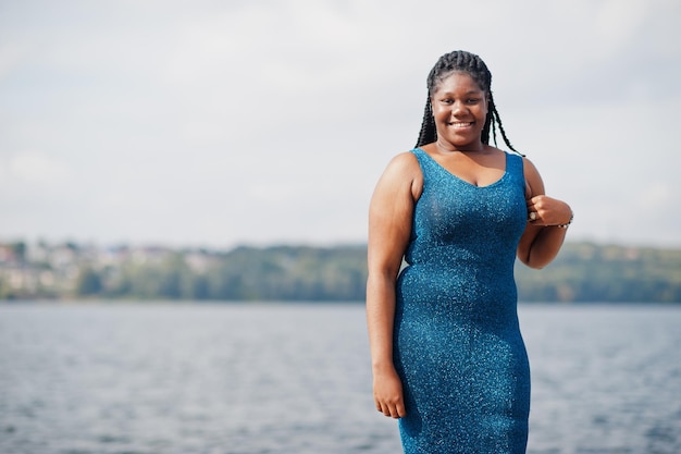 Afro-Amerikaans donkergevild plus size model poseerde in een blauwe glanzende jurk tegen de zeekant