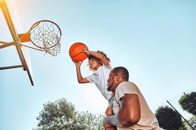 Afro-Amerikaans kind lacht en houdt een basketbal vast terwijl hij omhoog wordt geholpen door zijn ondersteunende vader