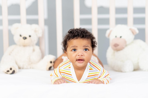 Afro-Amerikaans klein kind liggend in bed in oranje kleren met zachte beren