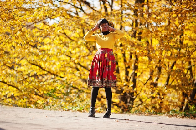 Afro-Amerikaans meisje bij gele en rode jurk in het gouden herfstpark