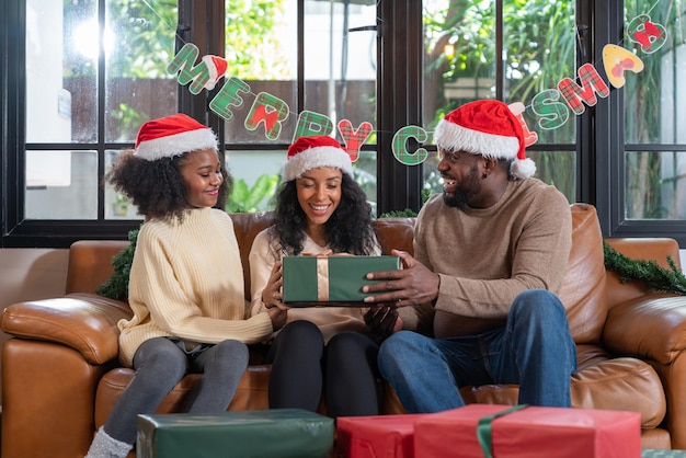 Afro-Amerikaans meisje dat haar vader of papa binnenshuis een geschenkdoos geeft met Merry Christmas