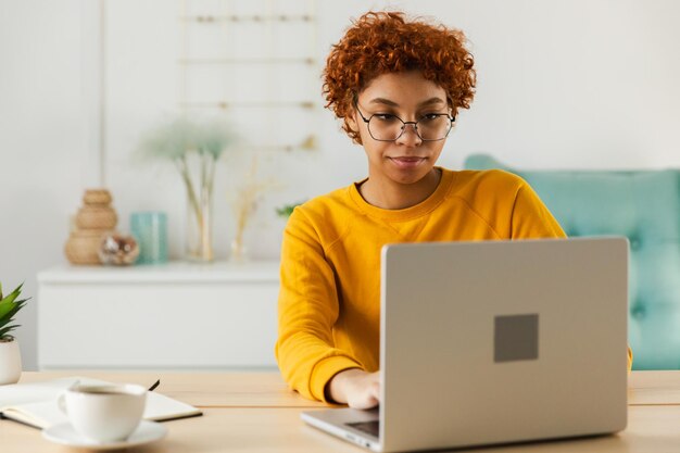 Afro-Amerikaans meisje dat laptop gebruikt op kantoor, naar het scherm kijkt, schrijft, chatteert, leest en schrijft.