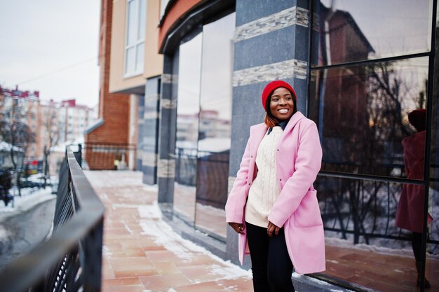 Afro-Amerikaans meisje in rode hoed en roze jas op straat van de stad tegen het voortbouwen op winterdag