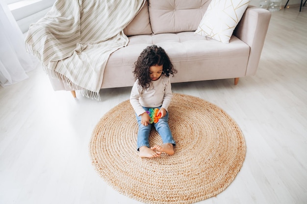 Afro-Amerikaans meisje op de vloer thuis spelend met een pop-speeltje dat op knoppen drukt om stress te verlichten