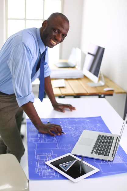 Afro-Amerikaanse architect werkt met computer en blauwdrukken op kantoor