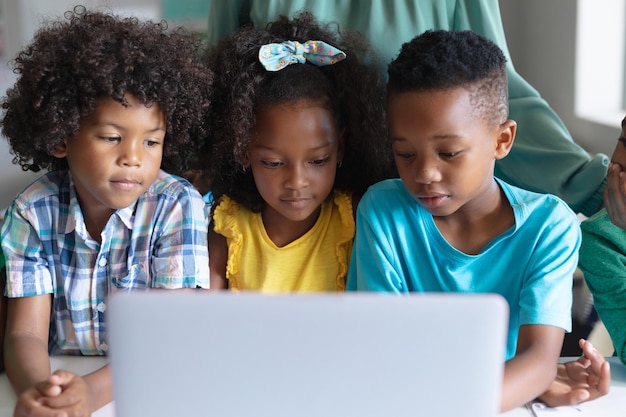 Afro-Amerikaanse basisscholieren gebruiken een laptop terwijl ze tijdens de computerles aan het bureau zitten