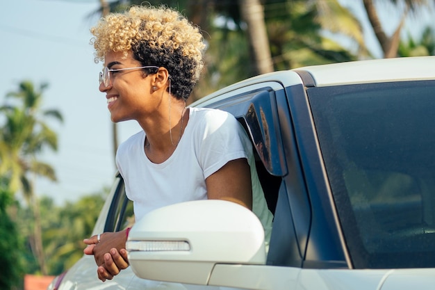 Afro-Amerikaanse blonde krullend haar meisje met mooie heldere tanden zittend in haar auto op tropische reis