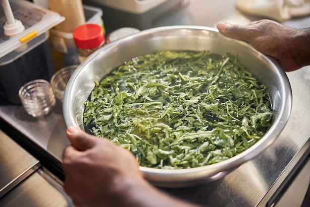 Afro-Amerikaanse chef-kok met kom met groen en water op tafel