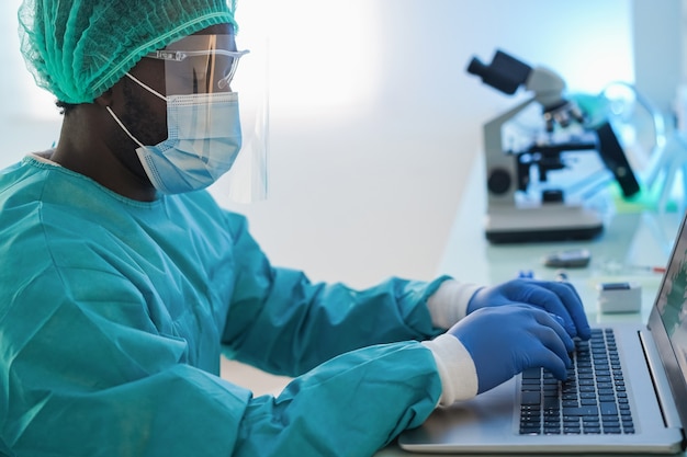 Afro-Amerikaanse dokter man met behulp van computer laptop met veiligheidsmasker op het werk in het ziekenhuis - Focus op toetsenbord