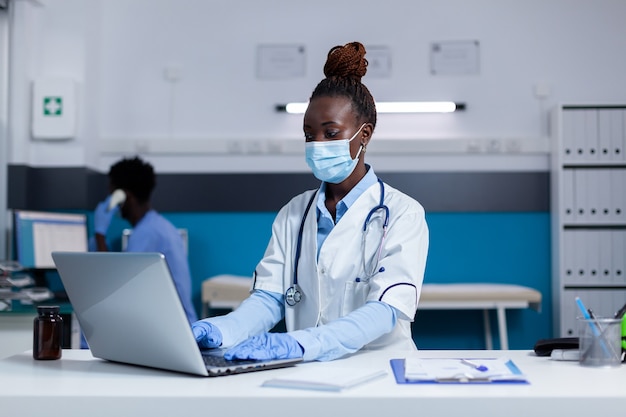 Afro-Amerikaanse dokter zit aan bureau met laptop