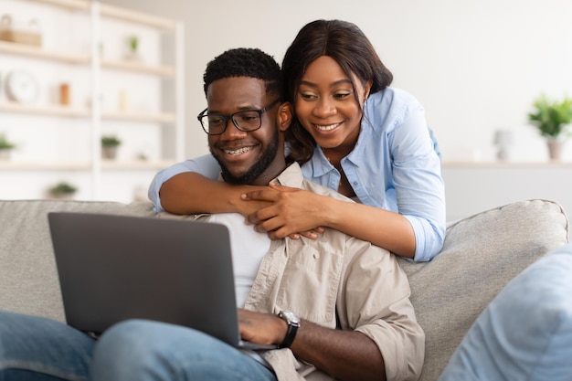 Afro-Amerikaanse echtpaar zittend op de bank met behulp van laptop