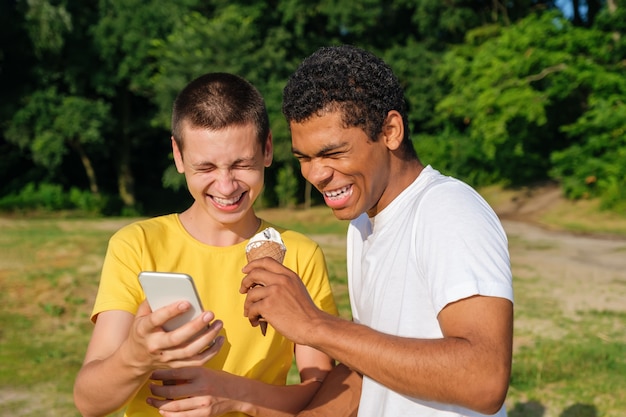 Afro-Amerikaanse en blanke vrienden eten ijs en gebruiken smartphone buiten