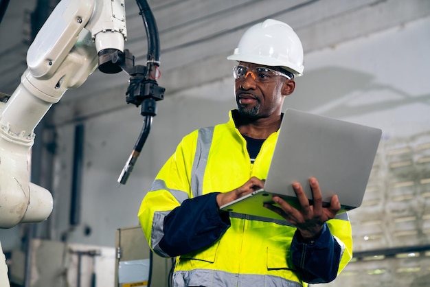 Afro-Amerikaanse fabrieksarbeider die werkt met een bedreven robotarm