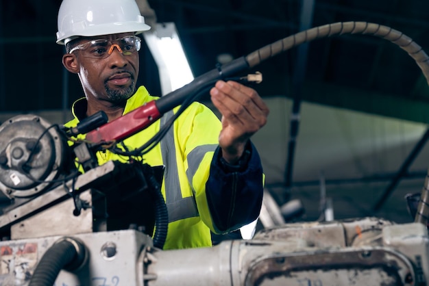 Afro-amerikaanse fabrieksarbeider die werkt met een bedreven robotarm