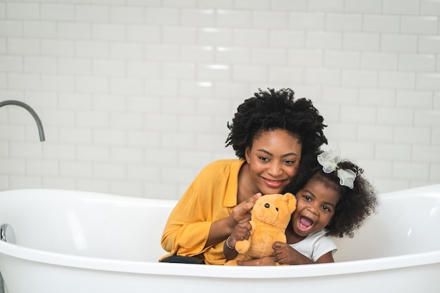 Afro-Amerikaanse familie, gelukkige moeder en dochtertje die plezier hebben en samen spelen in de badkamer, witte muurachtergrond