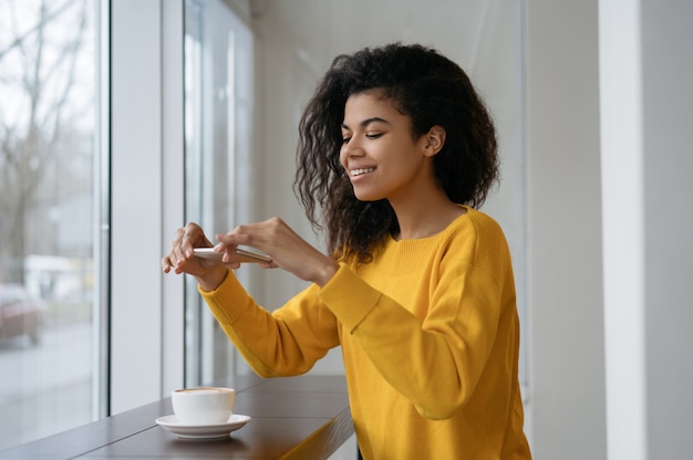 Afro-amerikaanse food blogger nemen foto op haar smartphone, zittend in café.