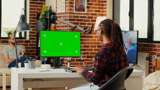 Afro-amerikaanse freelancer kijkt naar computer met greenscreen-sjabloon, werkt met lege copyspace chromakey. analyseren van pc-desktop met geïsoleerde mockup-achtergrond op monitor in kantoorruimte.