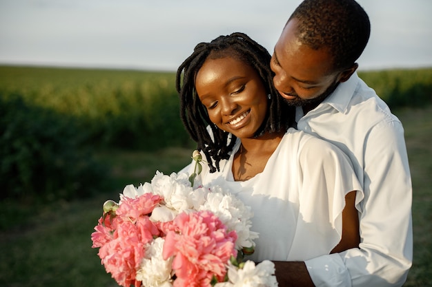 Afro-Amerikaanse geliefden omarmen in een veld. Vrouw met bloemen.