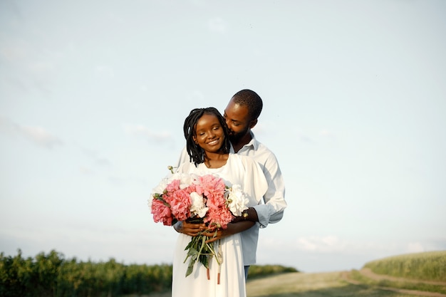 Afro-Amerikaanse geliefden omarmen in een veld. Vrouw met bloemen.