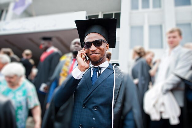 Afro-Amerikaanse gelukkige man bij afstuderen Afgestudeerde student die telefoon spreekt bij mensenmassa