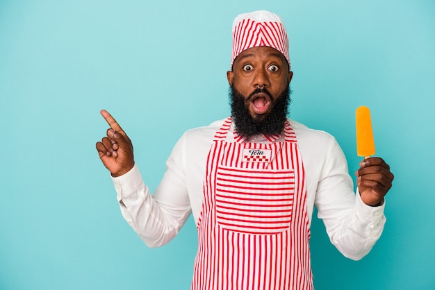 Afro-Amerikaanse ijsmaker man met een ijsje geïsoleerd op blauwe achtergrond wijzend naar de zijkant