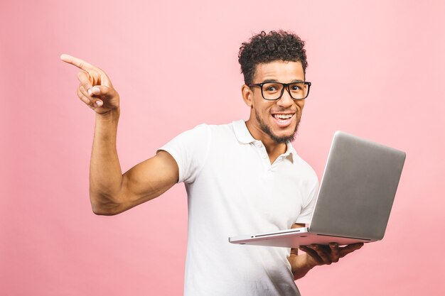 Afro-Amerikaanse jonge man met laptop over geïsoleerde roze achtergrond verrast
