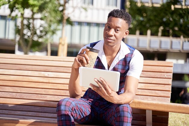 Afro-Amerikaanse jonge man met tabletcomputer en koffie mee te nemen