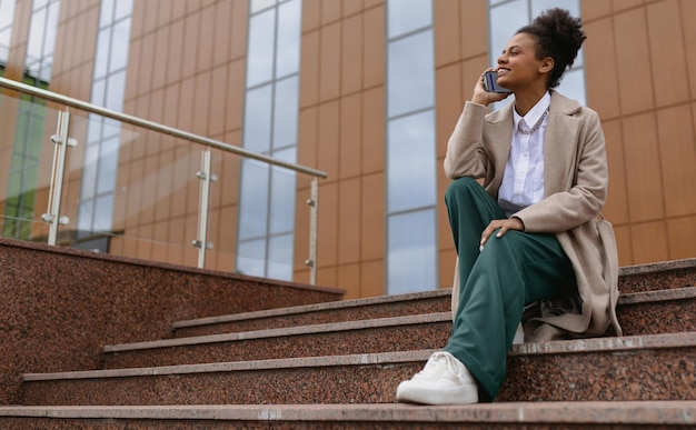 Afro-Amerikaanse jonge vrouw die aan de telefoon praat terwijl ze op de trap zit tegen de achtergrond van