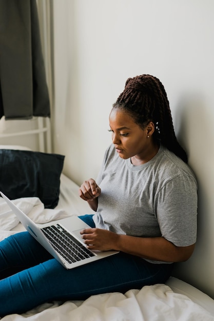 Afro-Amerikaanse jonge vrouw die laptop op bedtechnologieën en communicatie en sociaal netwerk gebruikt