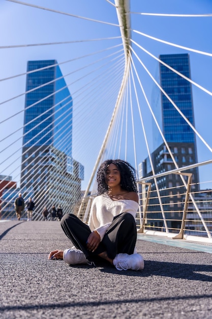 Afro-Amerikaanse jonge vrouw in het stadsportret van een jonge vrouw die lachend op een brug zit