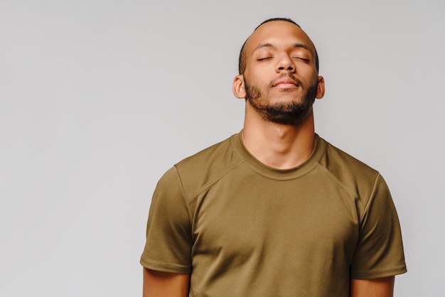 Afro-Amerikaanse jongeman in groen t-shirt over lichtgrijze muur met ogen gesloten met lege ruimte