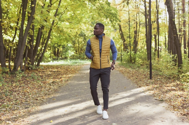 Afro-Amerikaanse jongeman wandelingen in herfst park op warme zonnige dag