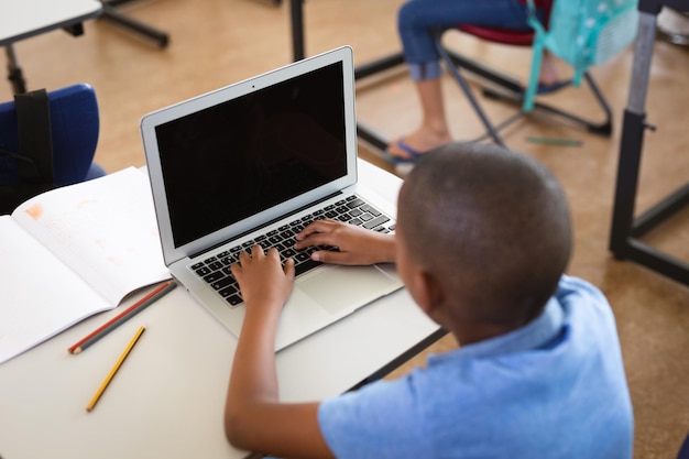 Afro-Amerikaanse jongen die laptop gebruikt terwijl hij op zijn bureau zit in de klas op de basisschool