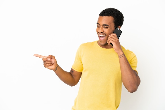 Afro-amerikaanse knappe man die mobiele telefoon gebruikt over een geïsoleerde witte achtergrond die met de vinger naar de zijkant wijst en een product presenteert