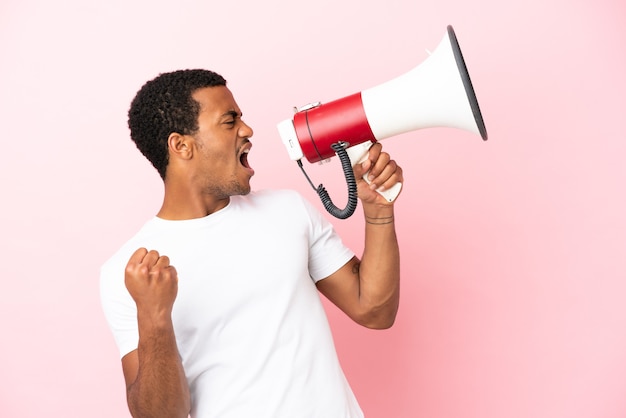 Afro-Amerikaanse knappe man op geïsoleerde roze achtergrond die door een megafoon schreeuwt om iets in zijpositie aan te kondigen