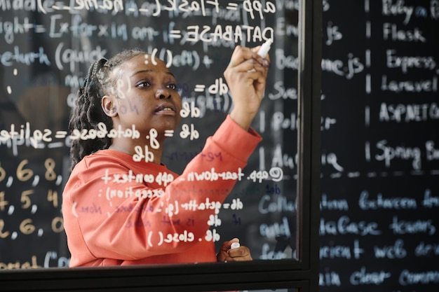 Afro-Amerikaanse leraar schrijft codes op het bord. Ze geeft les op school.