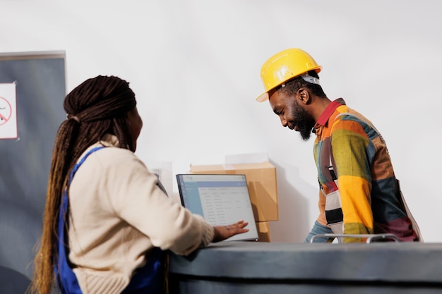 Afro-Amerikaanse magazijncollega's chatten aan de balie terwijl ze de factuurlijst op de computer controleren. Alle medewerkers van het zwarte magazijn kijken naar de checklist van klanten voor orderpicking