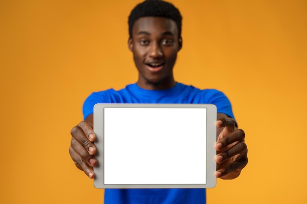 Afro-Amerikaanse man die een leeg digitaal tabletscherm toont met kopieerruimte in gele studio