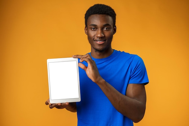 Afro-Amerikaanse man die een leeg digitaal tabletscherm toont met kopieerruimte in gele studio