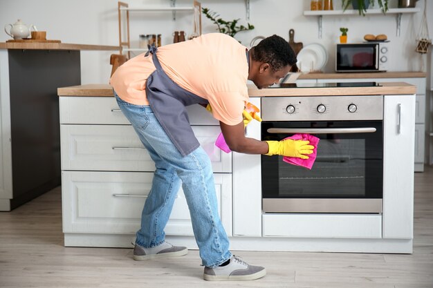 Afro-Amerikaanse man die oven in keuken schoonmaakt