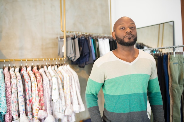 Afro-Amerikaanse man gaat mannelijke overhemden in de winkel kopen. Ernstige jonge man die in de buurt van hangers staat met kleding die naar de camera kijkt en wacht op hulp van winkelbedienden. Nieuw herenkleding- en modeconcept kopen