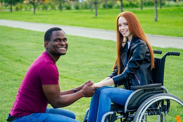 Afro-Amerikaanse man huwelijksaanzoek geeft een ring aan zijn roodharige gember vriendin. Ze zit op een rolstoel en verrast en verbaasd.