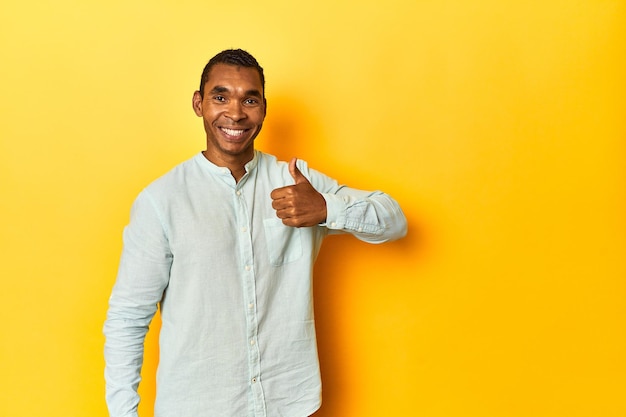 Afro-Amerikaanse man in blauw shirt gele studio glimlachend en duim omhoog