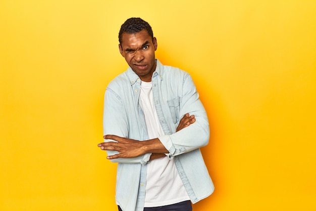 Afro-Amerikaanse man in blauw shirt gele studio ongelukkig kijken in de camera met sarcastische uitdrukking