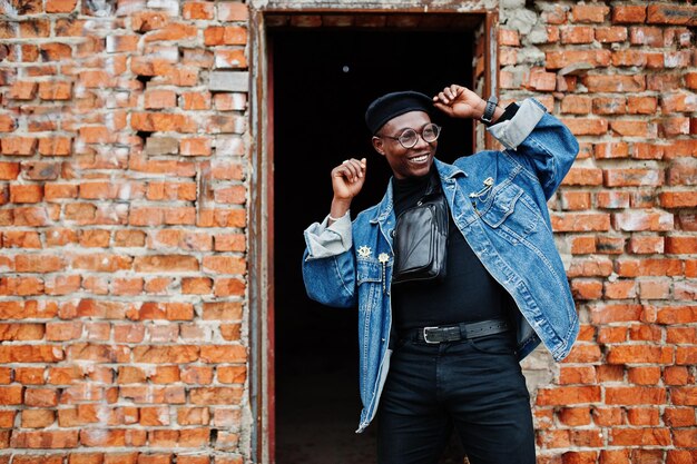 Afro-Amerikaanse man in jeans jasje baret en bril tegen bakstenen muur op verlaten dak