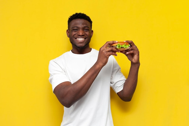 Afro-Amerikaanse man in wit T-shirt met een grote burger en glimlachend de man eet fastfood