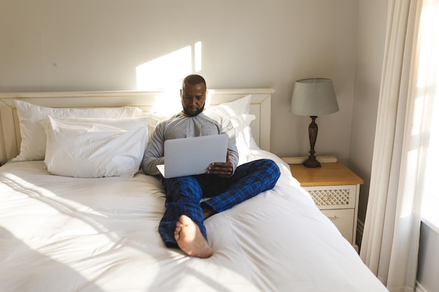 Afro-Amerikaanse man met behulp van laptop en liggend op bed in zijn slaapkamer