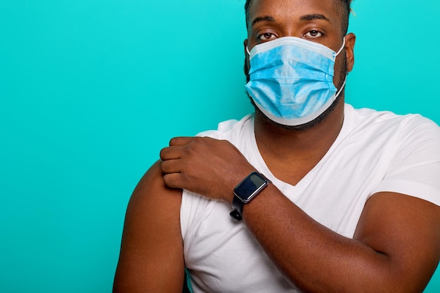 Afro-Amerikaanse man met een antiviraal masker bereidt zich voor om te worden gevaccineerd, trok de mouw van een wit T-shirt op tijdens vaccinatie tegen coronavirus en keurt de immunisatie van covid19 goed