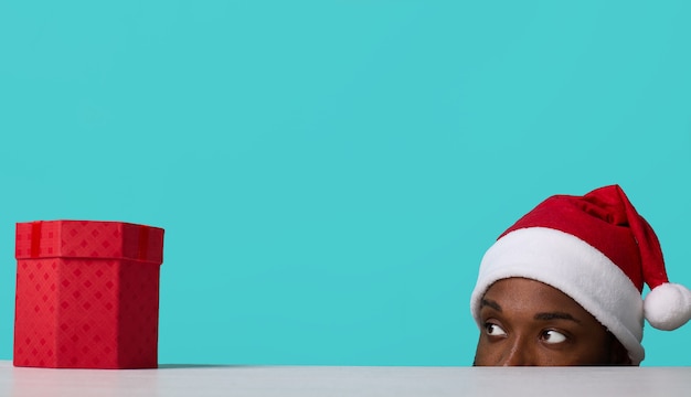 Afro-Amerikaanse man met kerstmuts kijkt naar een geschenk van onder de tafel